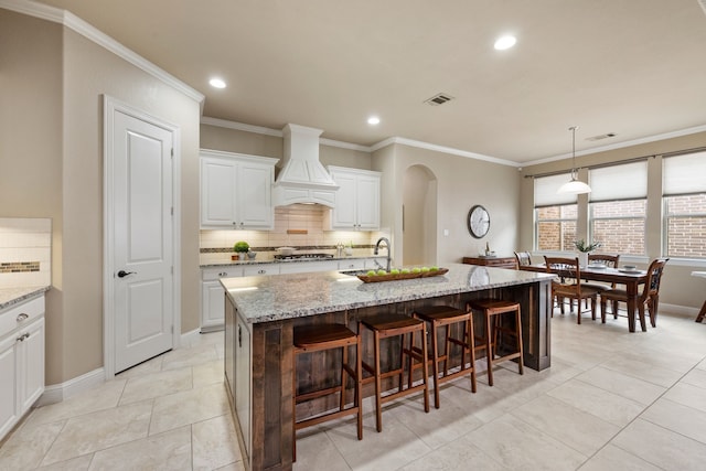 8240 Odell St, North Richland Hills, TX 76182 - kitchen featuring custom exhaust hood, decorative backsplash, stainless steel gas stovetop, arched walkways, and light stone counters