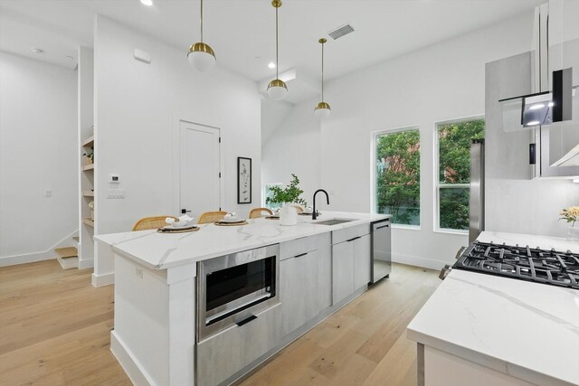 4208 Live Oak St Unit 102, Dallas, TX 75204 - kitchen featuring modern cabinets, stainless steel appliances, light wood-type flooring, an island with sink, and hanging light fixtures