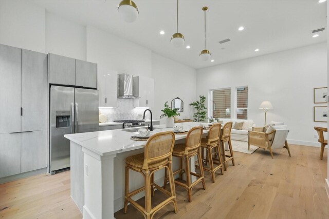 4208 Live Oak St Unit 102, Dallas, TX 75204 - kitchen with appliances with stainless steel finishes, wall chimney range hood, modern cabinets, a breakfast bar area, and light wood-style floors