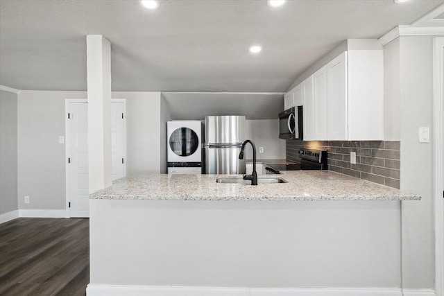 3620 Stadium Dr, Fort Worth, TX 76109 - kitchen featuring stainless steel appliances, stacked washing machine and dryer, a peninsula, decorative backsplash, and light stone counters