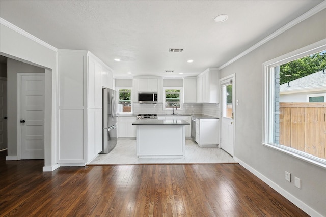 3620 Stadium Dr, Fort Worth, TX 76109 - kitchen with stainless steel appliances, light wood finished floors, white cabinets, backsplash, and ornamental molding