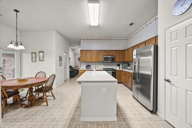 2918 Beau Dr, Mesquite, TX 75181 - kitchen featuring stainless steel appliances, brown cabinets, a textured ceiling, light countertops, and a kitchen island with sink