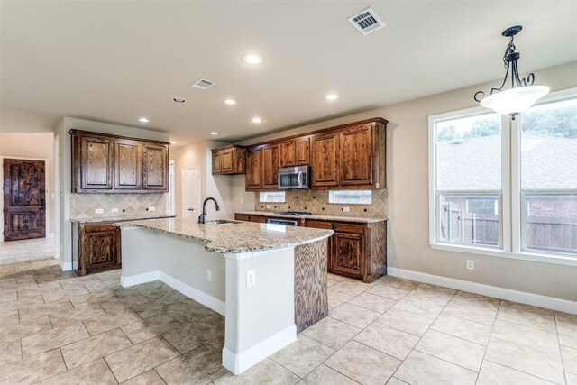 302 Shire Ln, Celina, TX 75009 - kitchen with stainless steel microwave, decorative backsplash, light stone counters, recessed lighting, and an island with sink