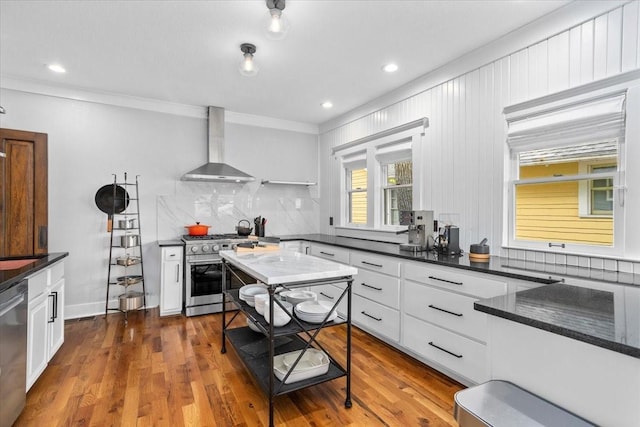 1600 S Adams St, Fort Worth, TX 76104 - kitchen featuring wall chimney range hood, stainless steel appliances, crown molding, white cabinetry, and backsplash