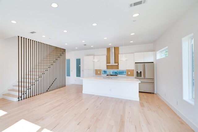 3821 Munger Ave Unit 105, Dallas, TX 75204 - kitchen with stainless steel fridge with ice dispenser, wall chimney range hood, light wood-style floors, white cabinets, and recessed lighting