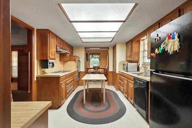 1419 Juniper Ln, Lewisville, TX 75077 - kitchen featuring black appliances, under cabinet range hood, light countertops, a textured ceiling, and brown cabinetry