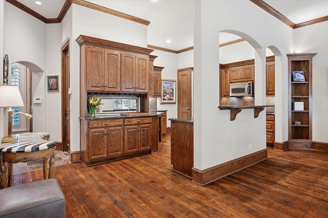 17227 Lechlade Ln, Dallas, TX 75252 - kitchen featuring stainless steel microwave, dark wood-style flooring, crown molding, arched walkways, and a breakfast bar