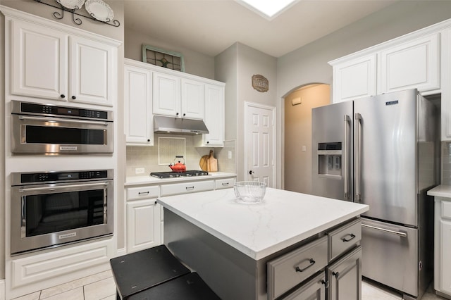 2413 Bachman Dr, Flower Mound, TX 75028 - kitchen with appliances with stainless steel finishes, under cabinet range hood, arched walkways, backsplash, and a center island