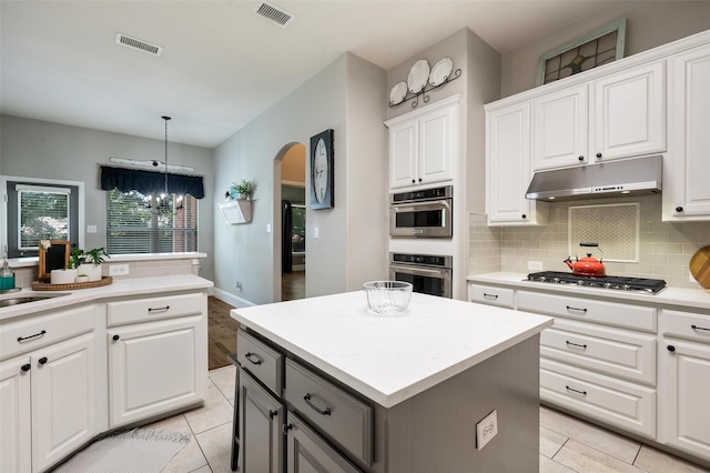 2413 Bachman Dr, Flower Mound, TX 75028 - kitchen featuring under cabinet range hood, stainless steel appliances, arched walkways, a kitchen island, and gray cabinetry