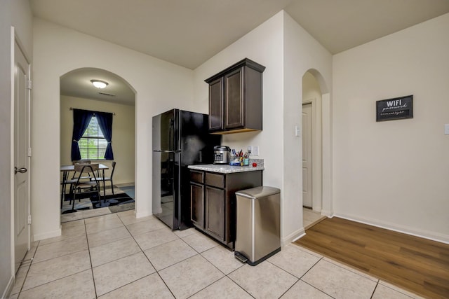 5921 Obsidian Creek Dr, Fort Worth, TX 76179 - kitchen featuring freestanding refrigerator, arched walkways, light tile patterned floors, and dark brown cabinetry
