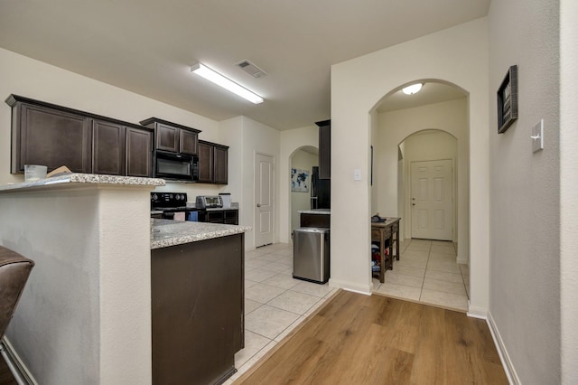 5921 Obsidian Creek Dr, Fort Worth, TX 76179 - kitchen with black appliances, arched walkways, dark brown cabinetry, and light tile patterned flooring