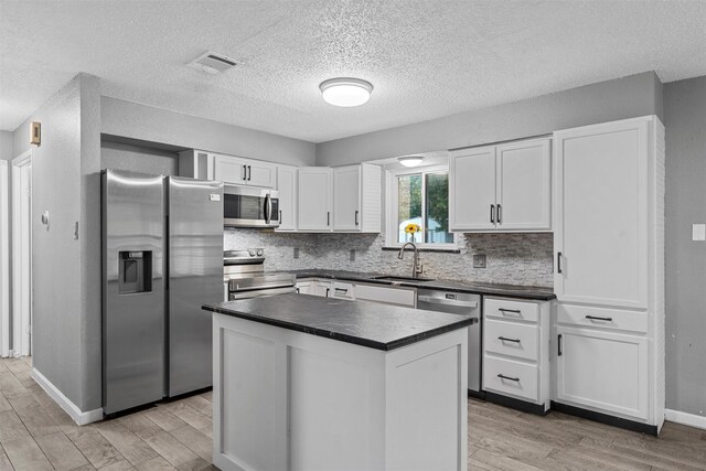 202 Lee Ln, Lorena, TX 76655 - kitchen with appliances with stainless steel finishes, dark countertops, light wood-type flooring, white cabinetry, and a textured ceiling