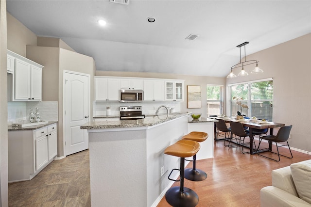 733 Atascosa Ave, Fort Worth, TX 76120 - kitchen featuring appliances with stainless steel finishes, lofted ceiling, decorative backsplash, white cabinets, and light stone counters