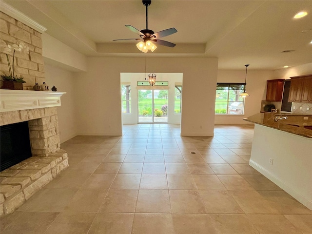 1413 Discovery Bay Dr, Frisco, TX 75036 - unfurnished living room featuring ceiling fan, a raised ceiling, light tile patterned floors, a stone fireplace, and recessed lighting