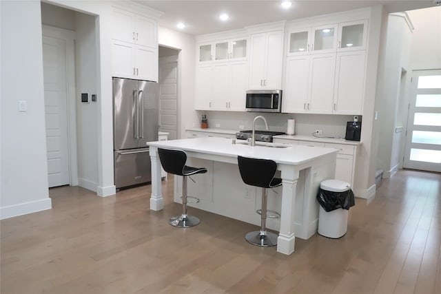 8327 Nunley Ln, Dallas, TX 75231 - kitchen featuring appliances with stainless steel finishes, light wood-style floors, light countertops, a breakfast bar area, and a kitchen island with sink