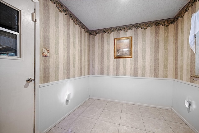 1803 Windsor Dr, Arlington, TX 76012 - spare room featuring wallpapered walls, a textured ceiling, tile patterned floors, and a wainscoted wall