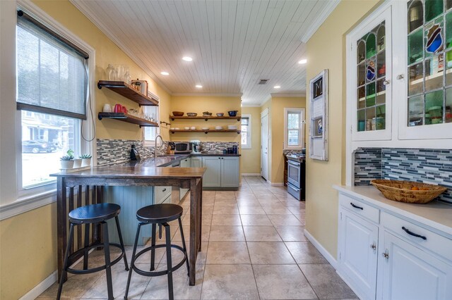 6201 Reiger Ave, Dallas, TX 75214 - kitchen featuring open shelves, stainless steel range with gas cooktop, crown molding, a breakfast bar area, and backsplash