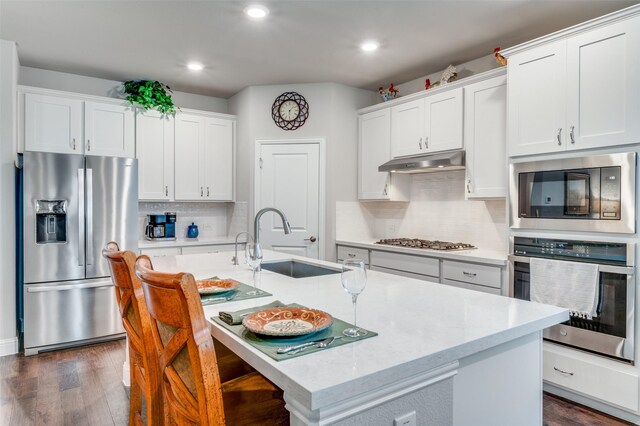 309 Savannah Ln, Oak Point, TX 75068 - kitchen featuring stainless steel appliances, under cabinet range hood, a kitchen island with sink, tasteful backsplash, and dark wood finished floors