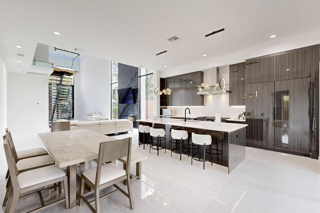 3828 Eaton Dr, Dallas, TX 75220 - kitchen featuring wall chimney range hood, modern cabinets, a kitchen bar, light countertops, and a center island with sink