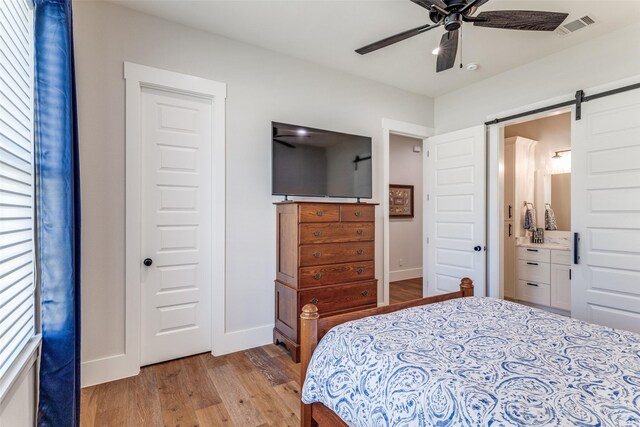 1757 Country Club Rd, Bowie, TX 76230 - bedroom with light wood-style floors, a barn door, ensuite bath, and a ceiling fan