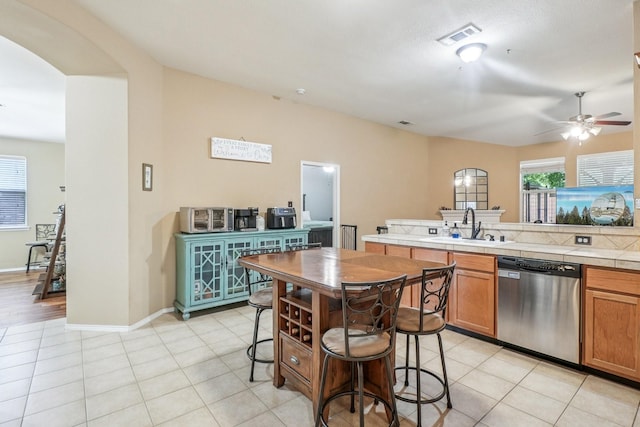 1323 Canyon Creek Rd, Wylie, TX 75098 - kitchen with stainless steel dishwasher, ceiling fan, tile countertops, arched walkways, and brown cabinetry