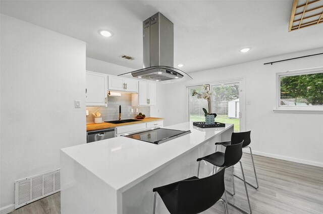 3105 Dupree St, Irving, TX 75062 - kitchen with island range hood, light wood finished floors, white cabinets, decorative backsplash, and a kitchen breakfast bar