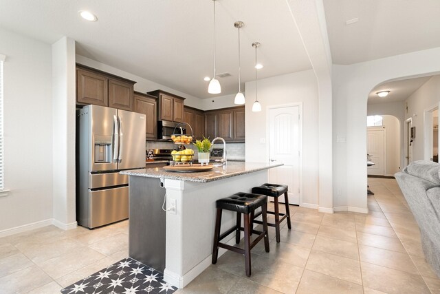 1112 Metaline Trl, Fort Worth, TX 76177 - kitchen featuring appliances with stainless steel finishes, arched walkways, a breakfast bar area, light stone countertops, and tasteful backsplash