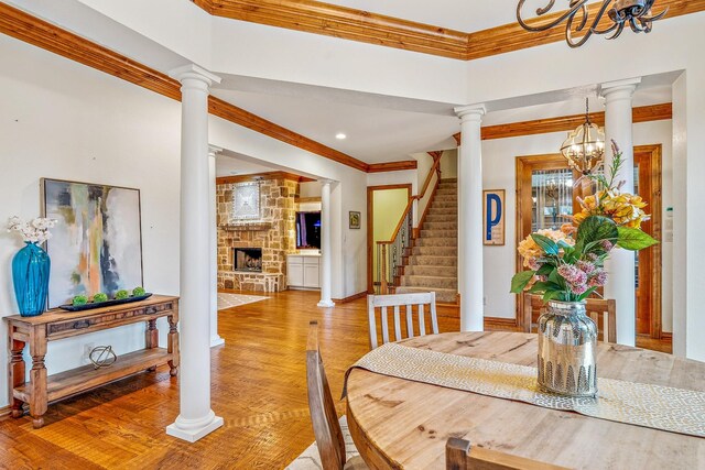 10133 Leaping Buck Pt, Fort Worth, TX 76126 - dining space with crown molding, a chandelier, a stone fireplace, light wood-style floors, and decorative columns