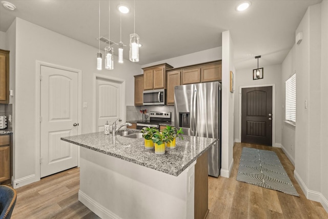 3109 Ethan Ln, Wylie, TX 75098 - kitchen with stainless steel appliances, light wood finished floors, a kitchen island with sink, brown cabinetry, and recessed lighting