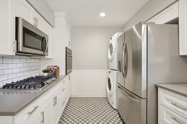 11335 Fernald Ave, Dallas, TX 75218 - kitchen with appliances with stainless steel finishes, stacked washer / drying machine, wainscoting, white cabinetry, and decorative backsplash