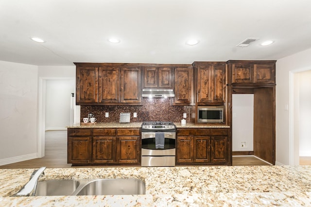 4410 Briargrove Ln, Dallas, TX 75287 - kitchen with stainless steel appliances, under cabinet range hood, backsplash, dark brown cabinets, and recessed lighting
