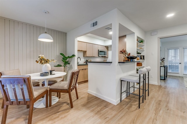 4239 Mckinney Ave Unit 202, Dallas, TX 75205 - kitchen featuring stainless steel microwave, dark countertops, light wood-style flooring, and a breakfast bar area