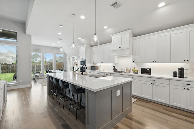 1110 Sandgate Dr, Forney, TX 75126 - kitchen with light wood-type flooring, a large island with sink, a kitchen bar, decorative backsplash, and light countertops
