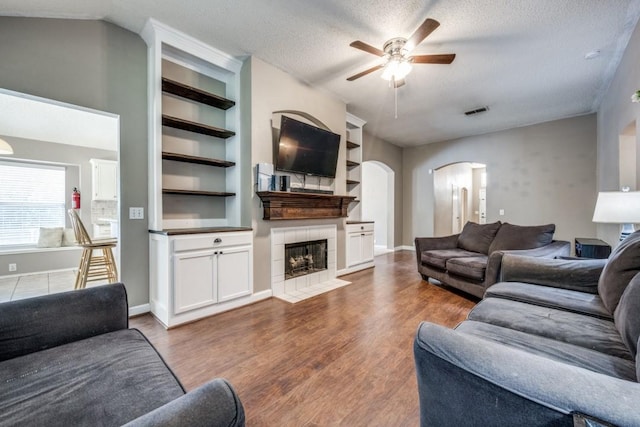 726 Texas Oak Trl, Lake Dallas, TX 75065 - living room with arched walkways, a ceiling fan, wood finished floors, a tiled fireplace, and a textured ceiling