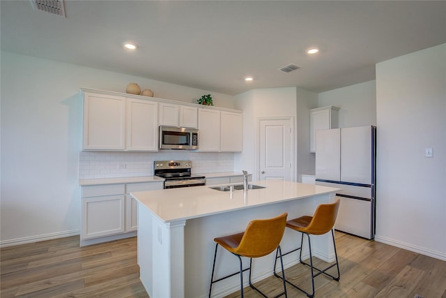 5221 Rockrose Ln, Princeton, TX 75407 - kitchen featuring stainless steel appliances, light wood-type flooring, white cabinetry, backsplash, and an island with sink