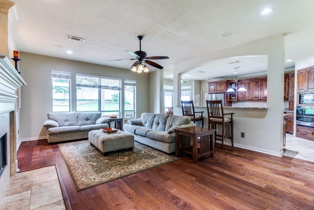6707 Canyon Crest Dr, Fort Worth, TX 76132 - living room with hardwood / wood-style flooring, a fireplace with flush hearth, arched walkways, a ceiling fan, and a textured ceiling