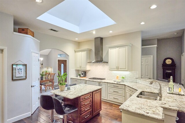 5513 Hill Haven Ct, Frisco, TX 75035 - kitchen with wall chimney exhaust hood, a peninsula, a kitchen breakfast bar, dark wood-style floors, and backsplash
