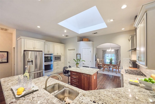 5513 Hill Haven Ct, Frisco, TX 75035 - kitchen featuring stainless steel appliances, a kitchen island, dark wood finished floors, arched walkways, and light stone countertops