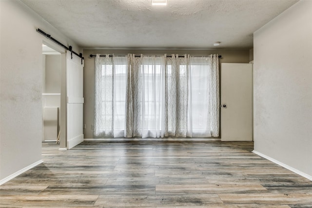 1614 Baltimore Dr, Richardson, TX 75081 - unfurnished room featuring a textured ceiling, a barn door, and wood finished floors