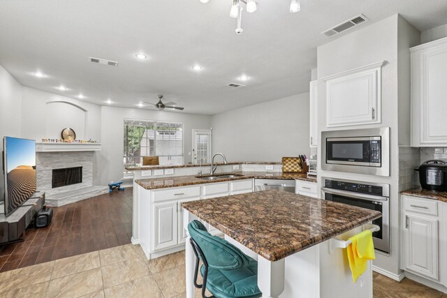 8729 Somerville Way, Plano, TX 75025 - kitchen featuring appliances with stainless steel finishes, a ceiling fan, open floor plan, a peninsula, and a stone fireplace