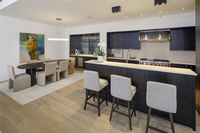 3626 Edgewater St, Dallas, TX 75205 - kitchen with wall chimney exhaust hood, light countertops, light wood-style floors, a breakfast bar area, and recessed lighting