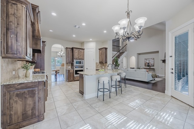 6913 Chisholm Trl, North Richland Hills, TX 76182 - kitchen with stainless steel appliances, a chandelier, arched walkways, a kitchen breakfast bar, and backsplash