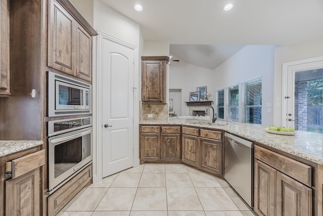 6913 Chisholm Trl, North Richland Hills, TX 76182 - kitchen featuring stainless steel appliances, light tile patterned flooring, light stone counters, decorative backsplash, and a fireplace