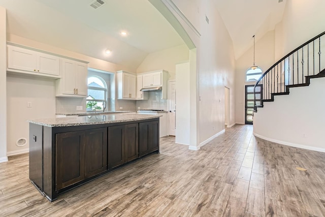 140 Godstone Ln, Prosper, TX 75078 - kitchen with white cabinetry, under cabinet range hood, light wood-style floors, decorative backsplash, and arched walkways