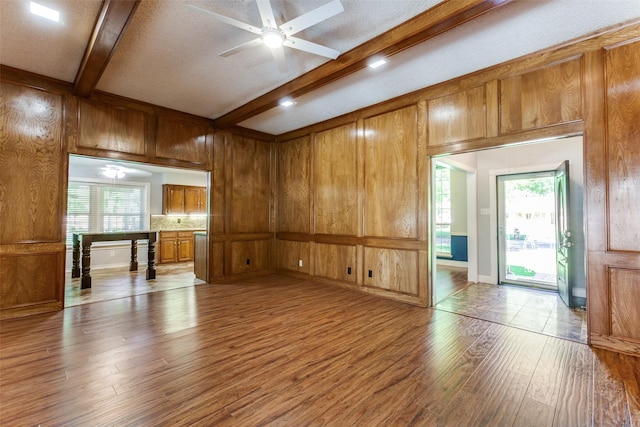 5008 Natchez Dr, Sachse, TX 75048 - unfurnished living room with wood finished floors, beam ceiling, wooden walls, ceiling fan, and a textured ceiling