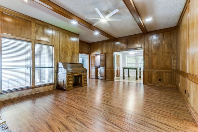 5008 Natchez Dr, Sachse, TX 75048 - unfurnished living room featuring ceiling fan, beamed ceiling, wooden walls, light wood finished floors, and a textured ceiling