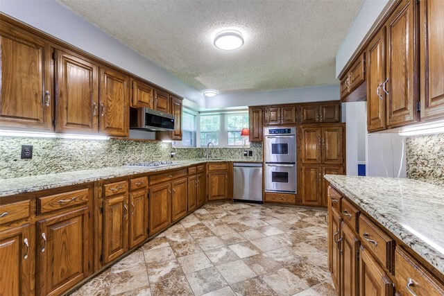 5008 Natchez Dr, Sachse, TX 75048 - kitchen with appliances with stainless steel finishes, a textured ceiling, brown cabinets, decorative backsplash, and light stone counters