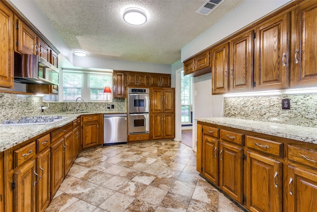 5008 Natchez Dr, Sachse, TX 75048 - kitchen with stainless steel appliances, brown cabinets, tasteful backsplash, a textured ceiling, and light stone countertops