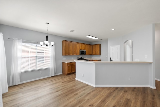 1205 Bonnet Dr, Fort Worth, TX 76131 - kitchen with stainless steel microwave, brown cabinetry, stove, arched walkways, and light wood-style flooring