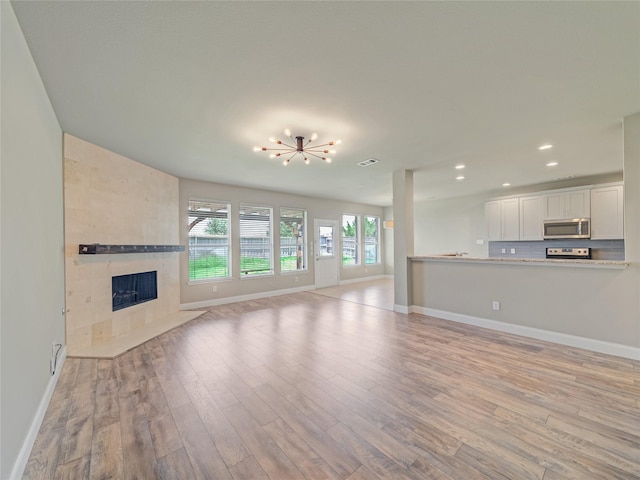 1034 Pelican Dr, Frisco, TX 75033 - unfurnished living room with light wood-style floors, recessed lighting, a fireplace, and a chandelier